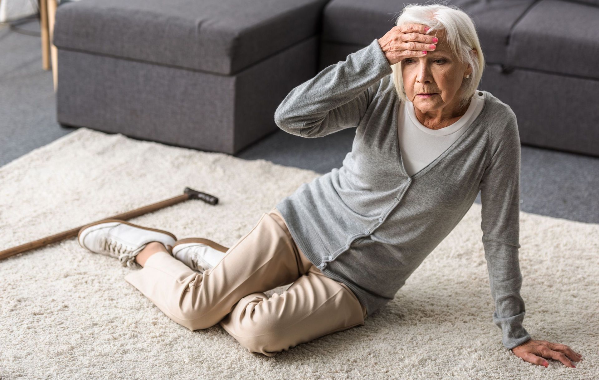 Senior Frau sitzt auf dem Teppich und hält sich die Stirn